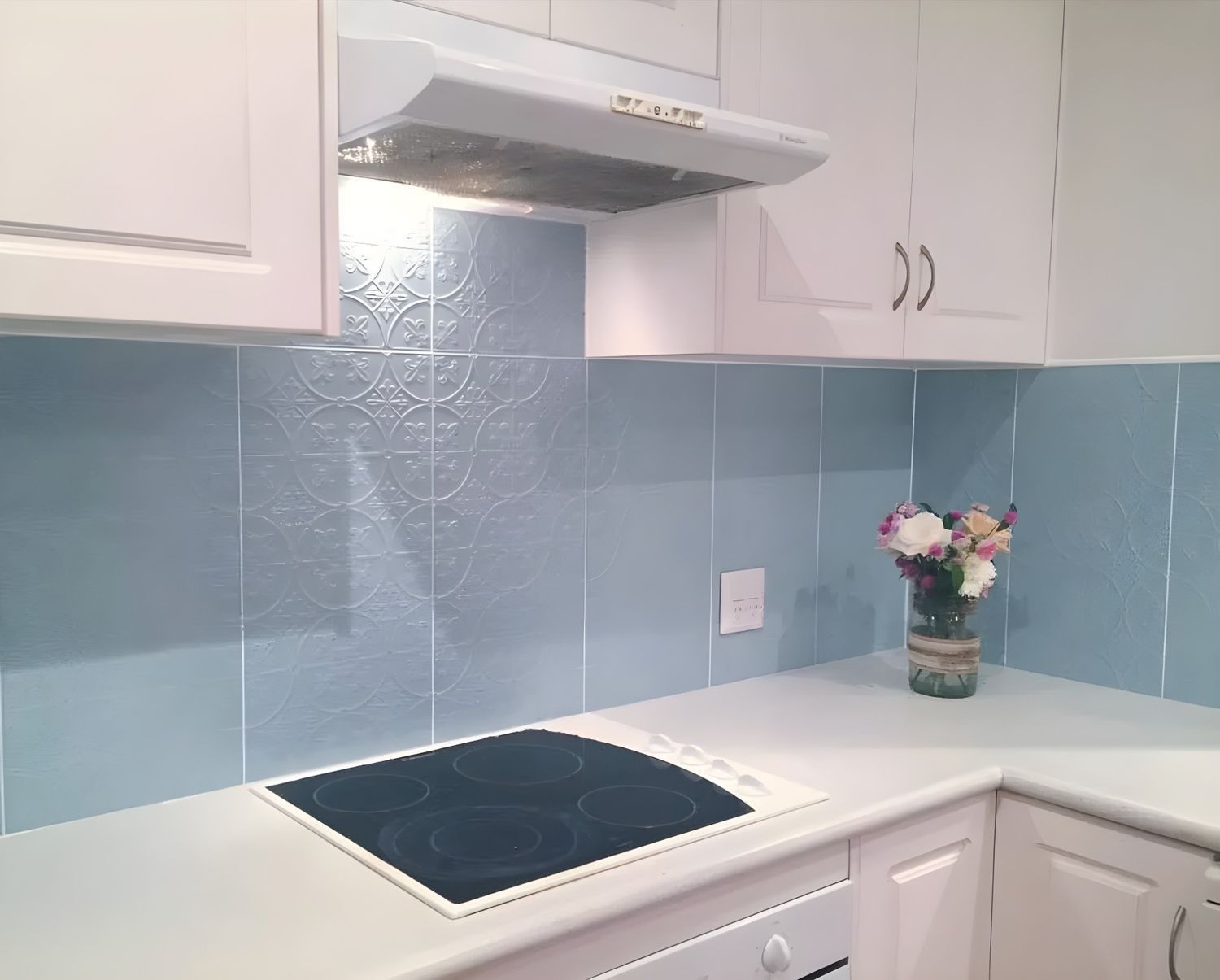 Light Blue Tiled Kitchen Backsplash, White Countertops and Cabinets, Electric Cooktop, and a Vase of Flowers — North Coast Tiles in Grafton, NSW
