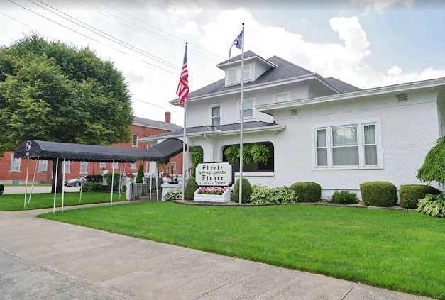 White Eberle-Fisher Funeral Home with American and Ohio flags. Black awning over entryway.