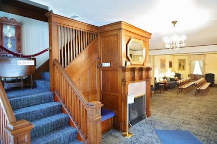 Wooden staircase leads up to a room with a fireplace, chairs, and a chandelier.