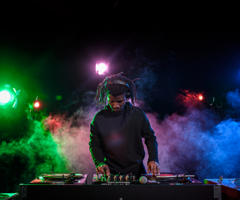 DJ mixing at a turntable amid green, pink, and blue stage smoke and lights