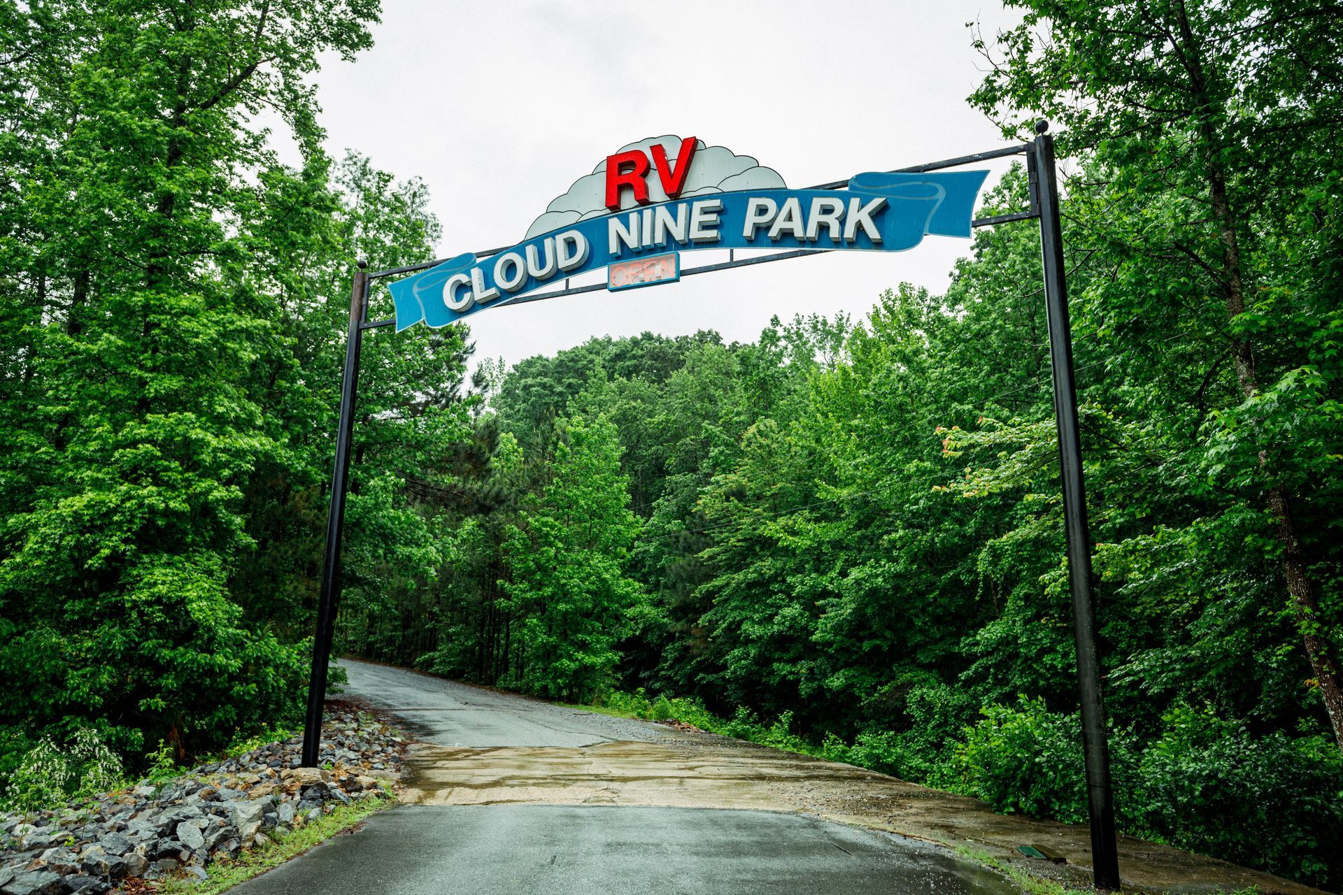 Cloud Nine Park entrance sign over a wooded path with a red-roofed building and red car logo