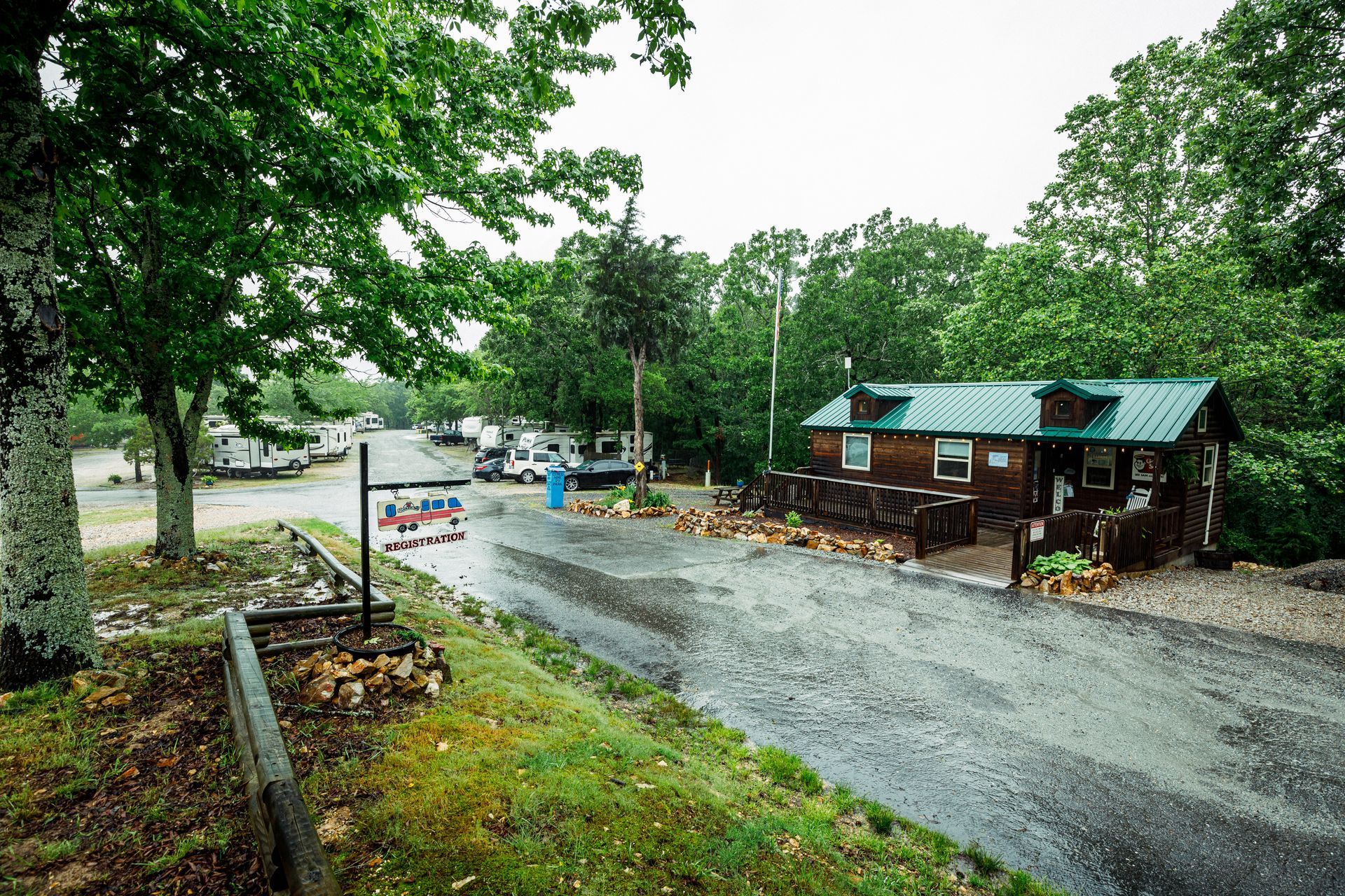 Rainy gravel road beside a small wooden cabin and trees in a rural area