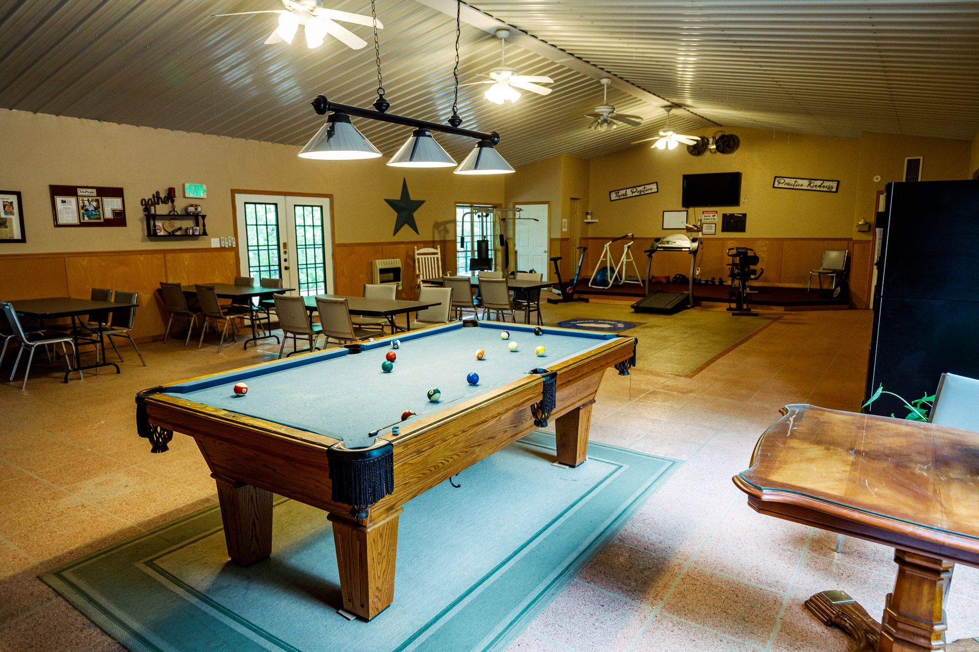 Spacious game room with a pool table, blue rug, and seating under warm ceiling lights.