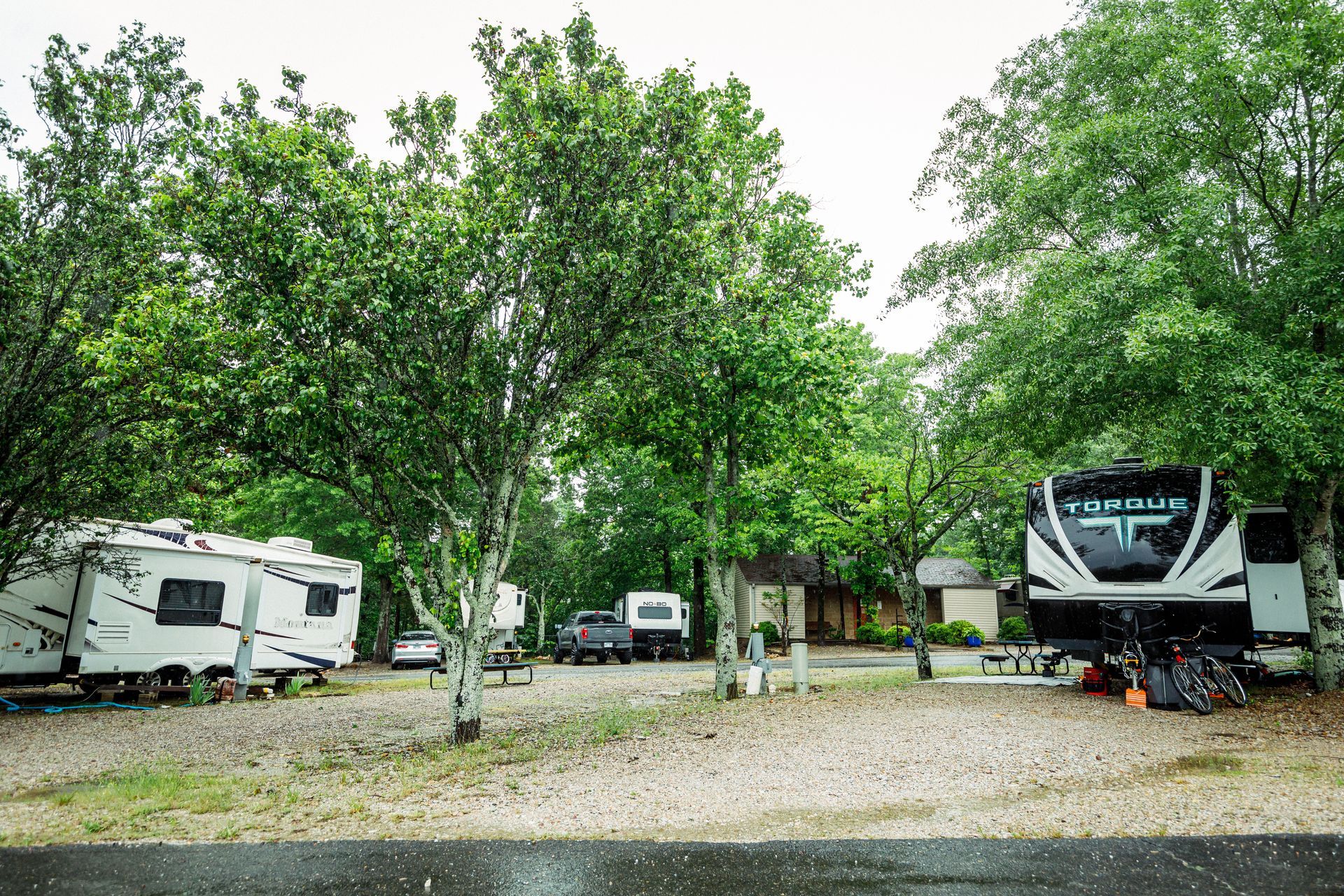 RV campground with several parked campers among tall green trees and gravel sites