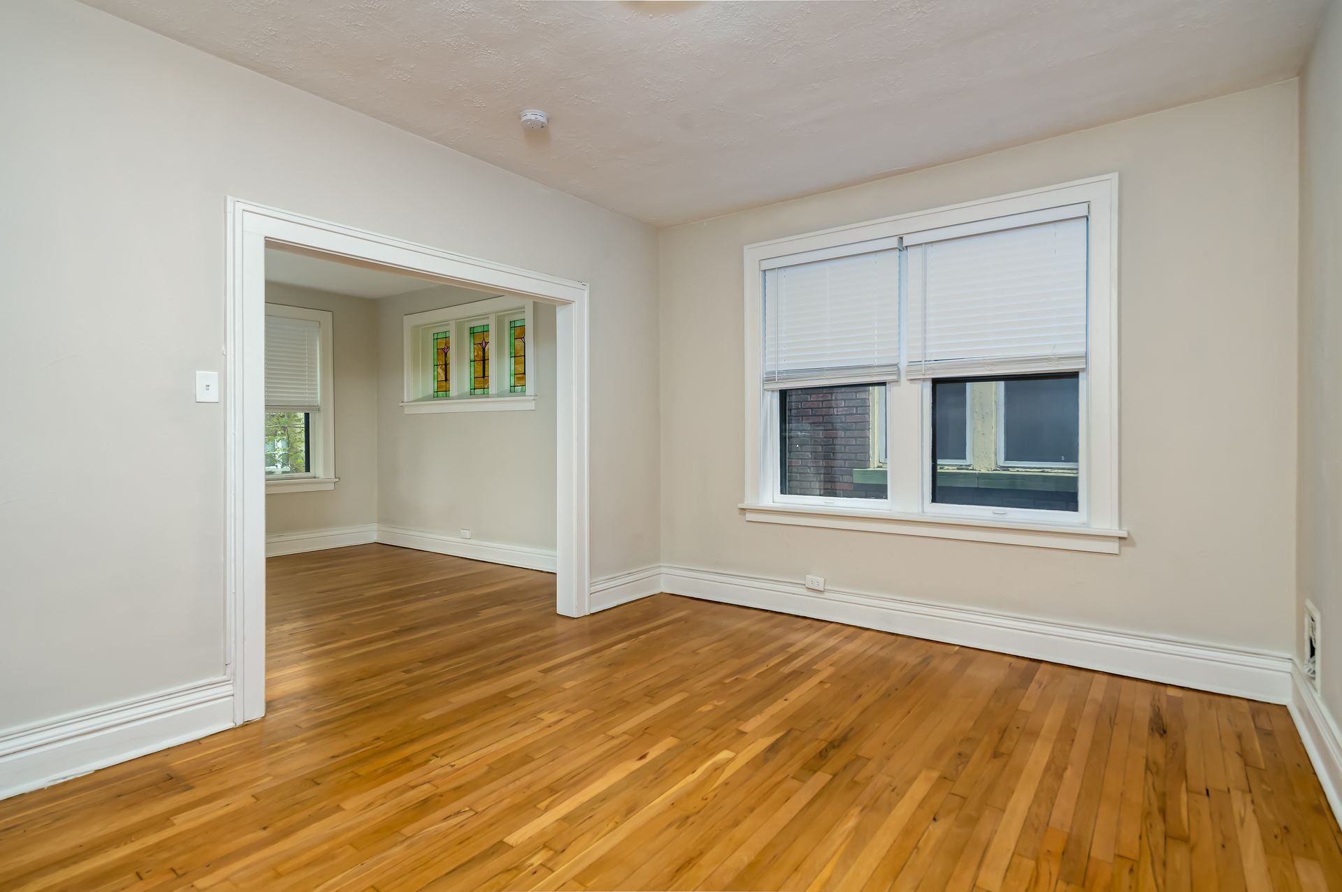 An empty living room with hardwood floors and two windows.