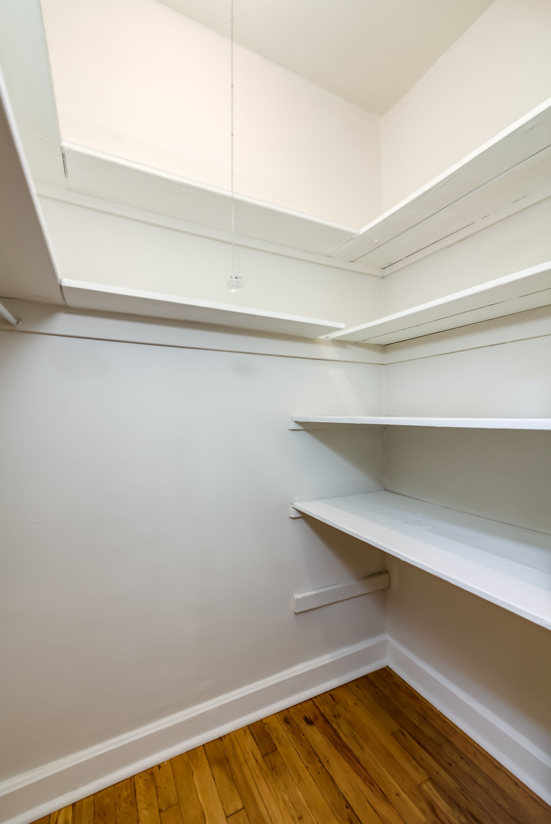 An empty walk in closet with hardwood floors and white shelves.