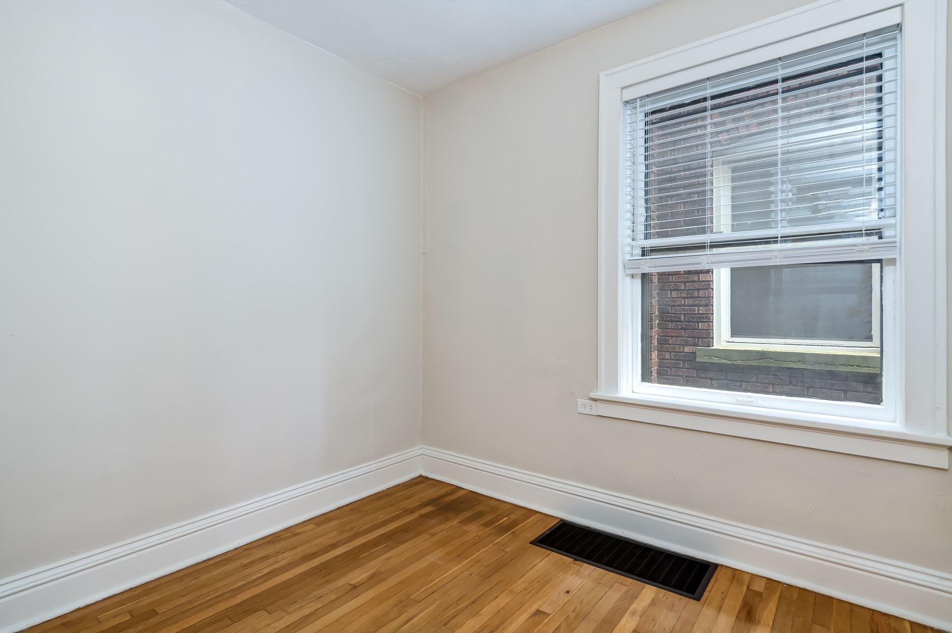 An empty room with hardwood floors and a window with blinds.