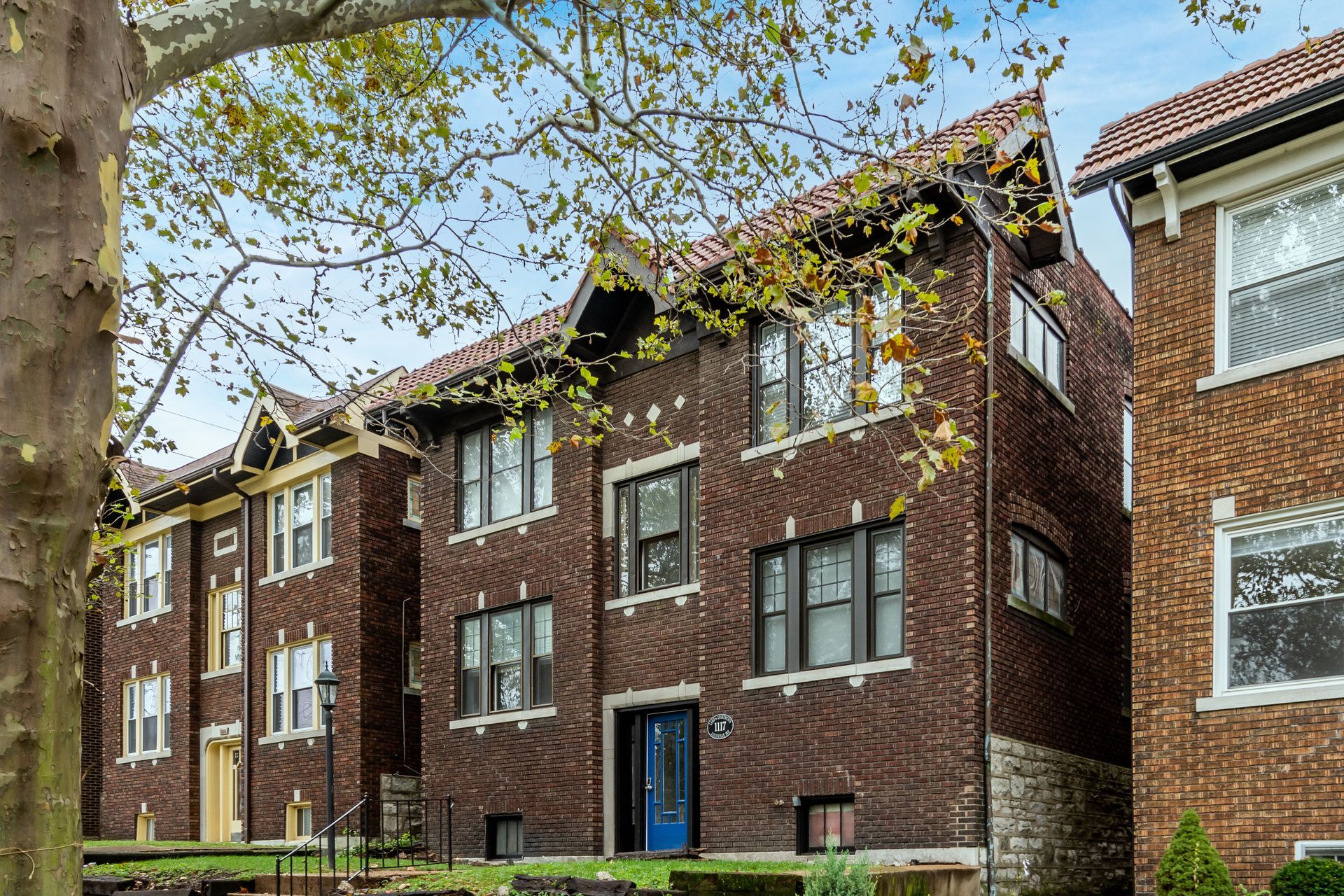 A brick apartment building with a blue door and a tree in front of it.