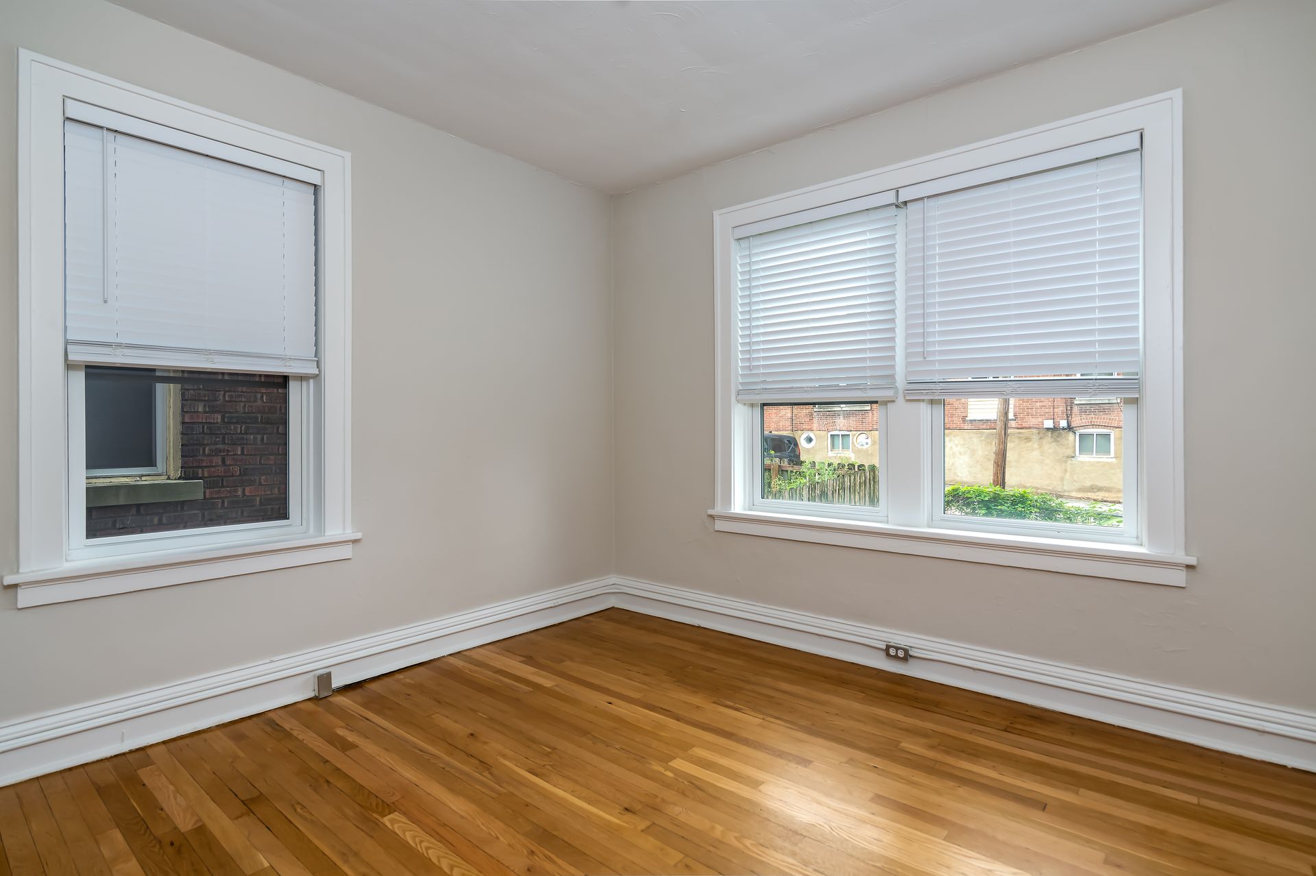 An empty room with hardwood floors and two windows with blinds.