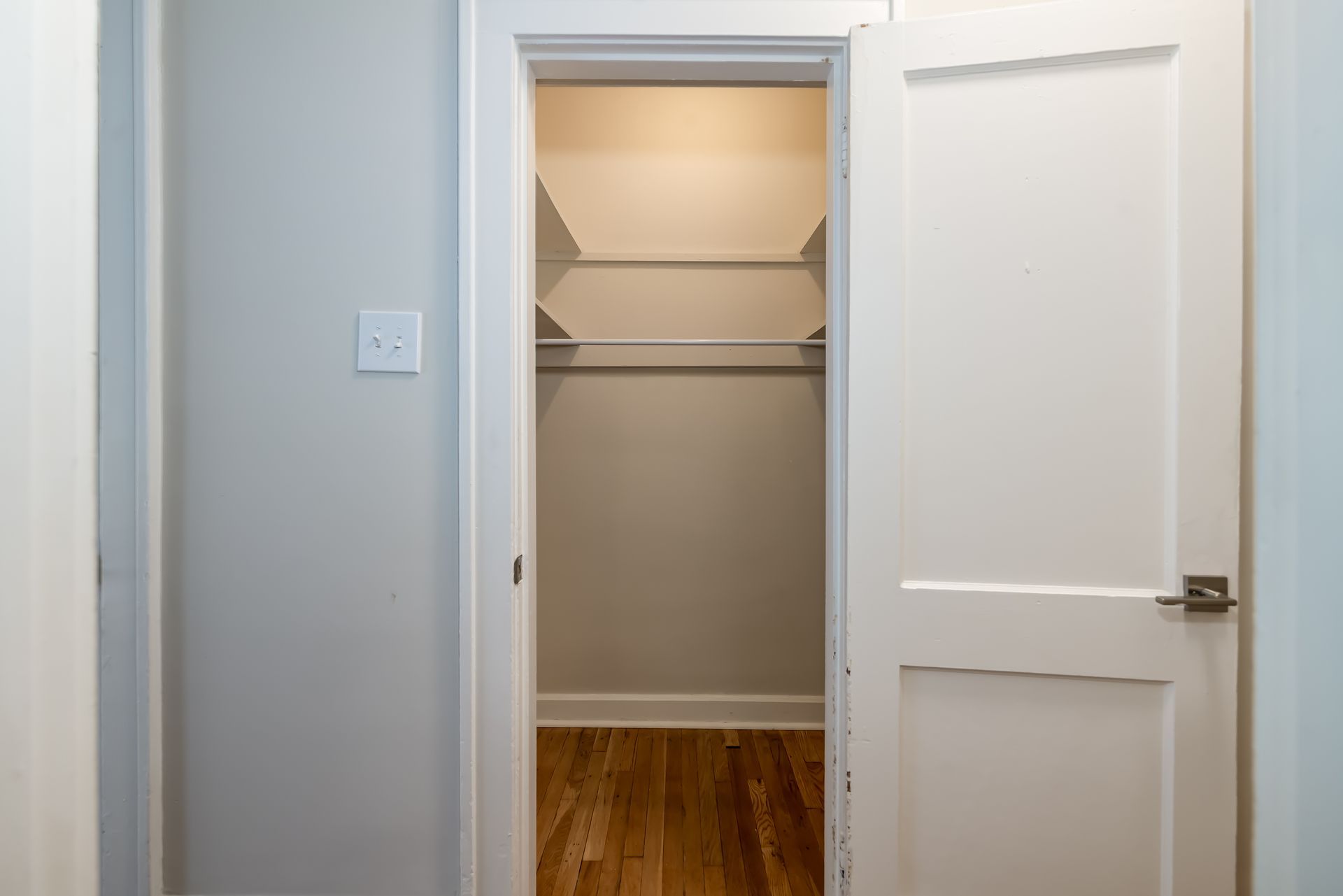 A walk in closet with hardwood floors and a white door.