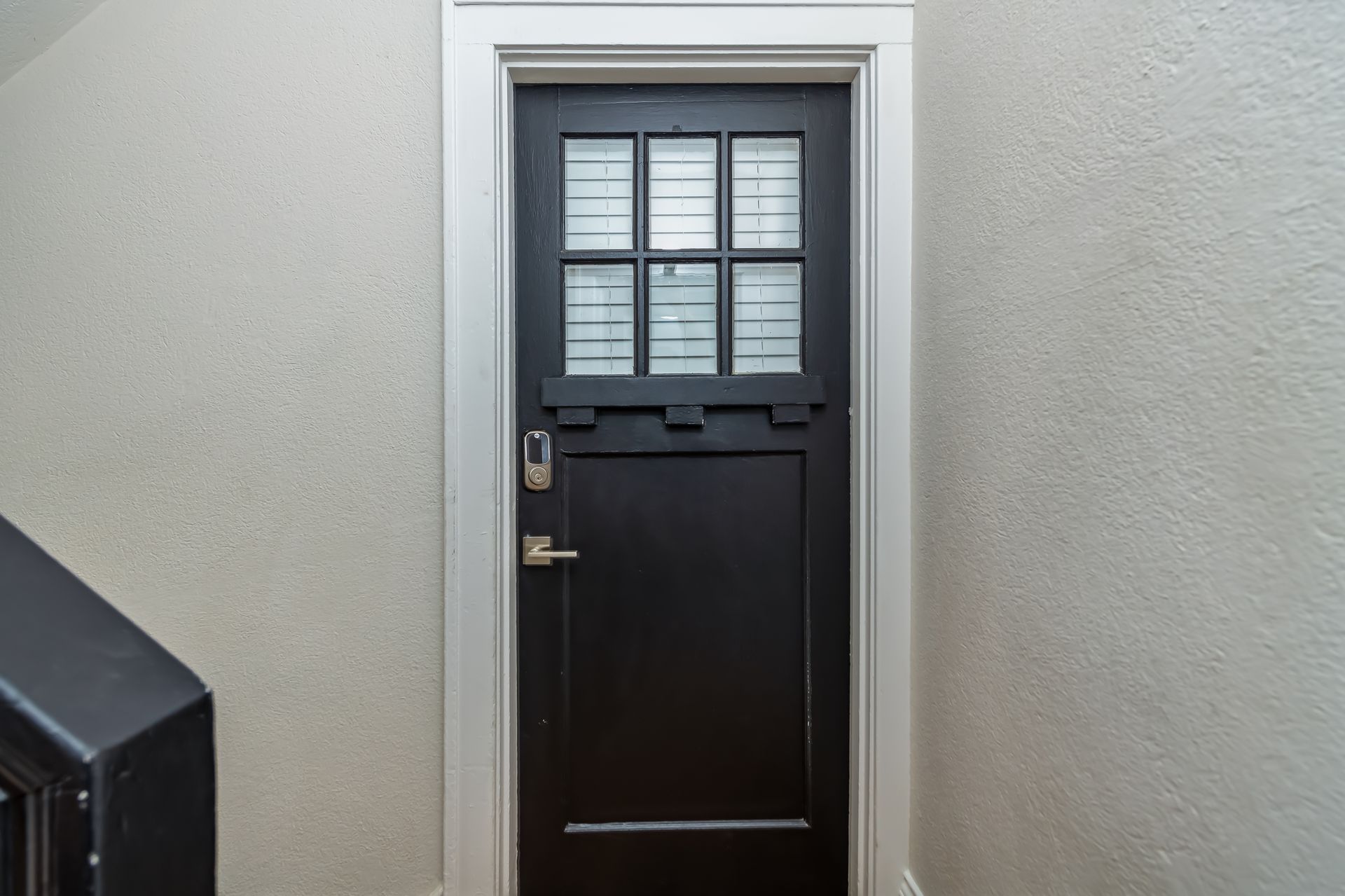 A black door with a glass window is on a white wall next to a staircase.
