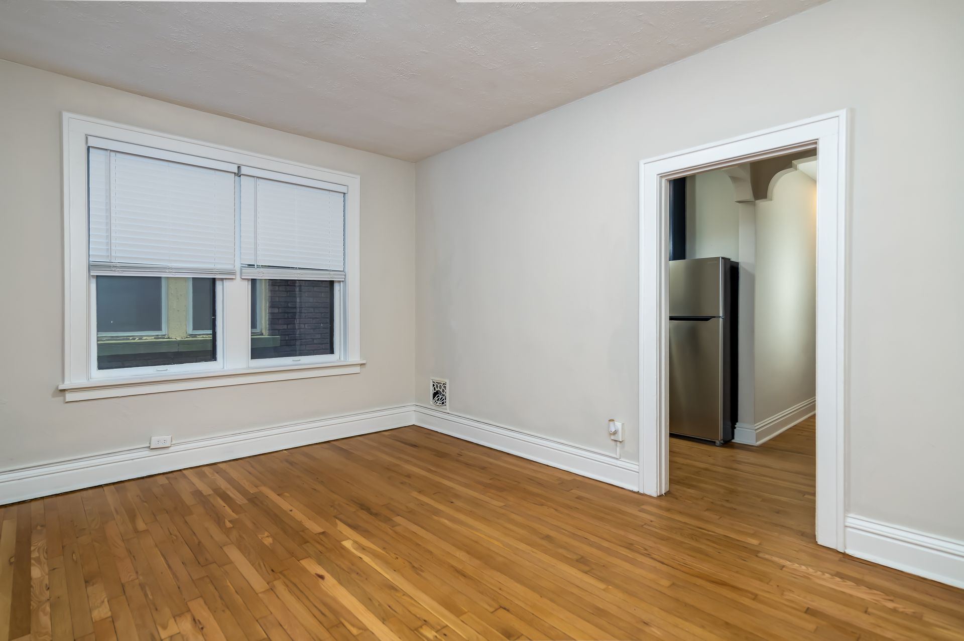 An empty room with hardwood floors and a refrigerator.