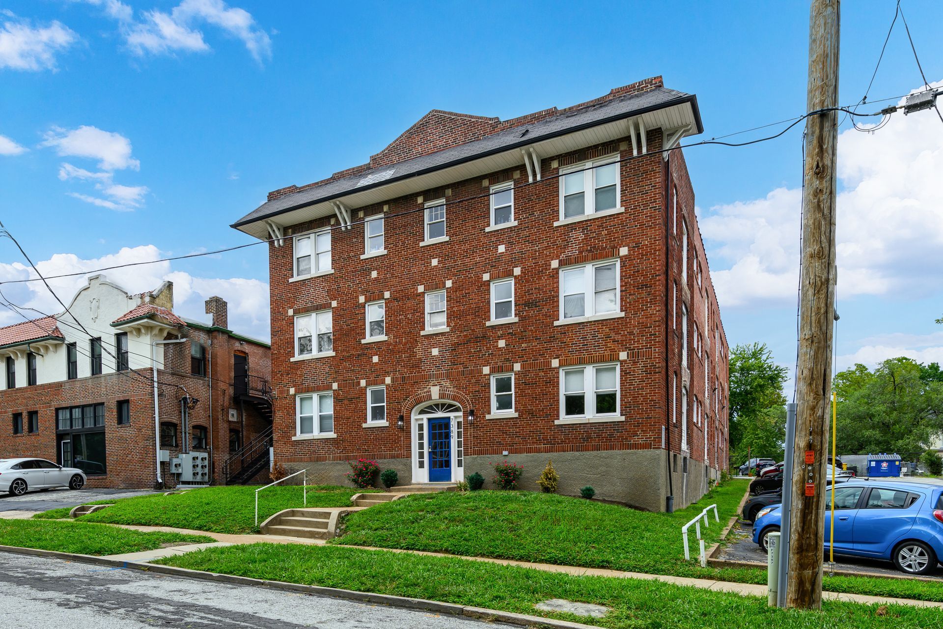 A brick apartment building with a blue door and a blue car parked in front of it.