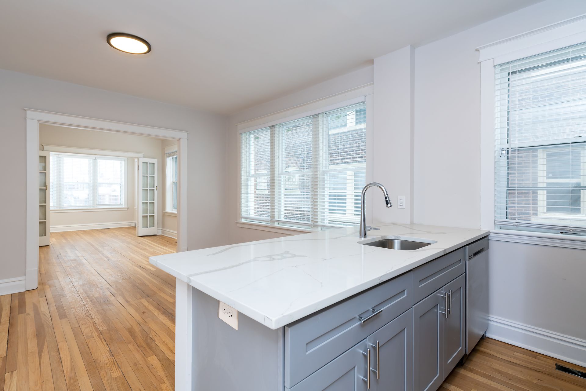 An empty kitchen with a sink , cabinets , and hardwood floors.