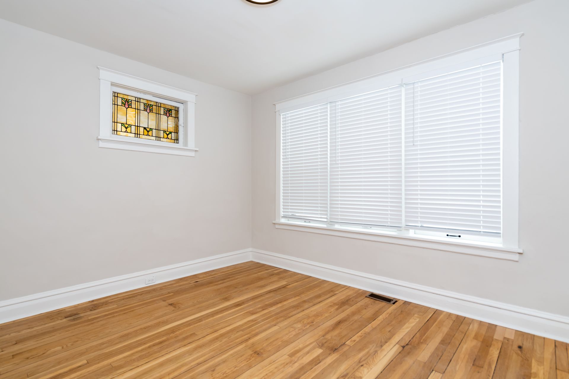 An empty room with hardwood floors and two windows.