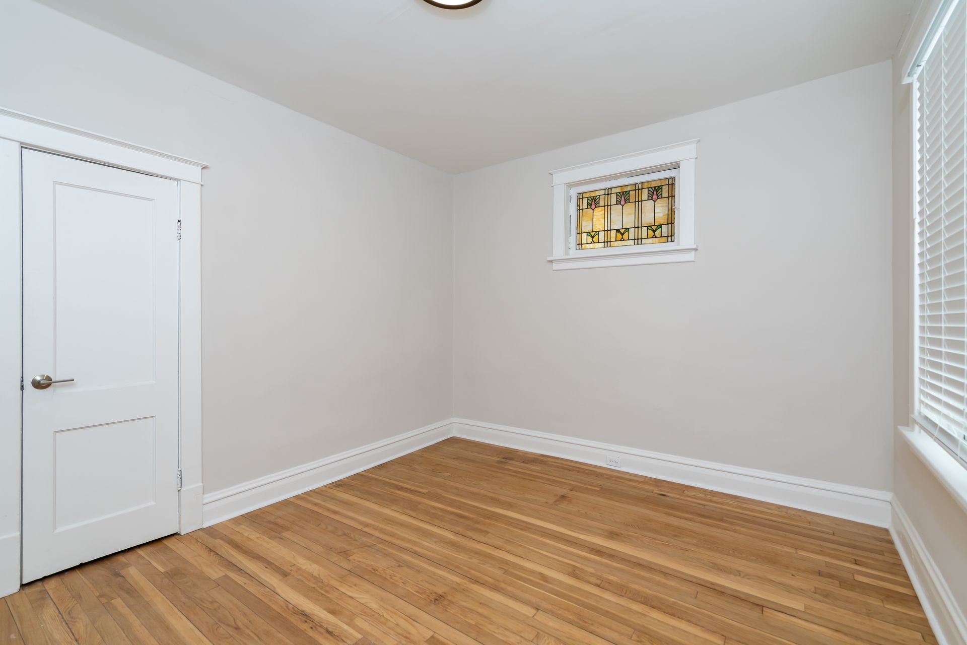 An empty room with hardwood floors , white walls and a window.