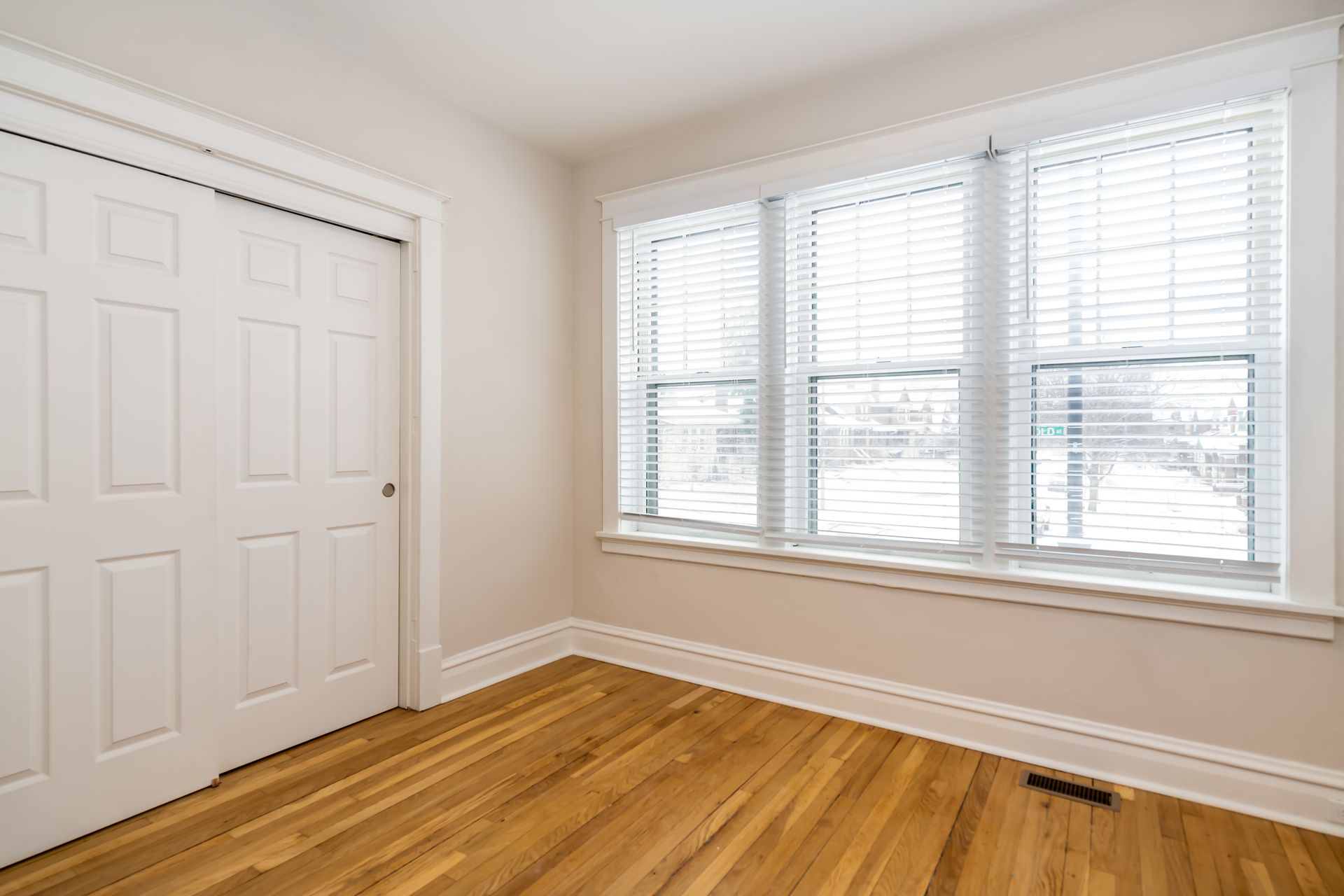 An empty bedroom with hardwood floors and white blinds.