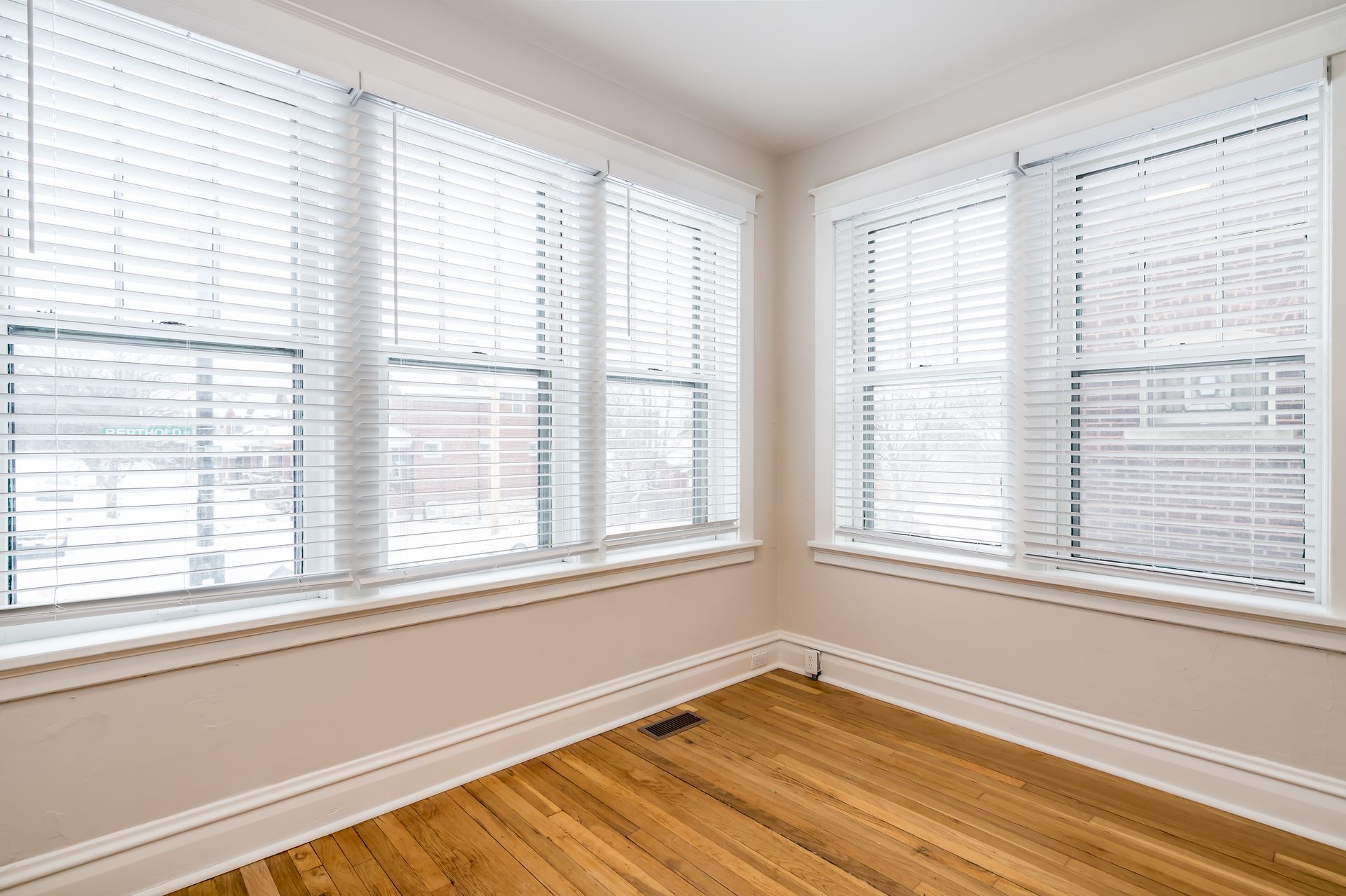 An empty room with hardwood floors and white blinds on the windows.