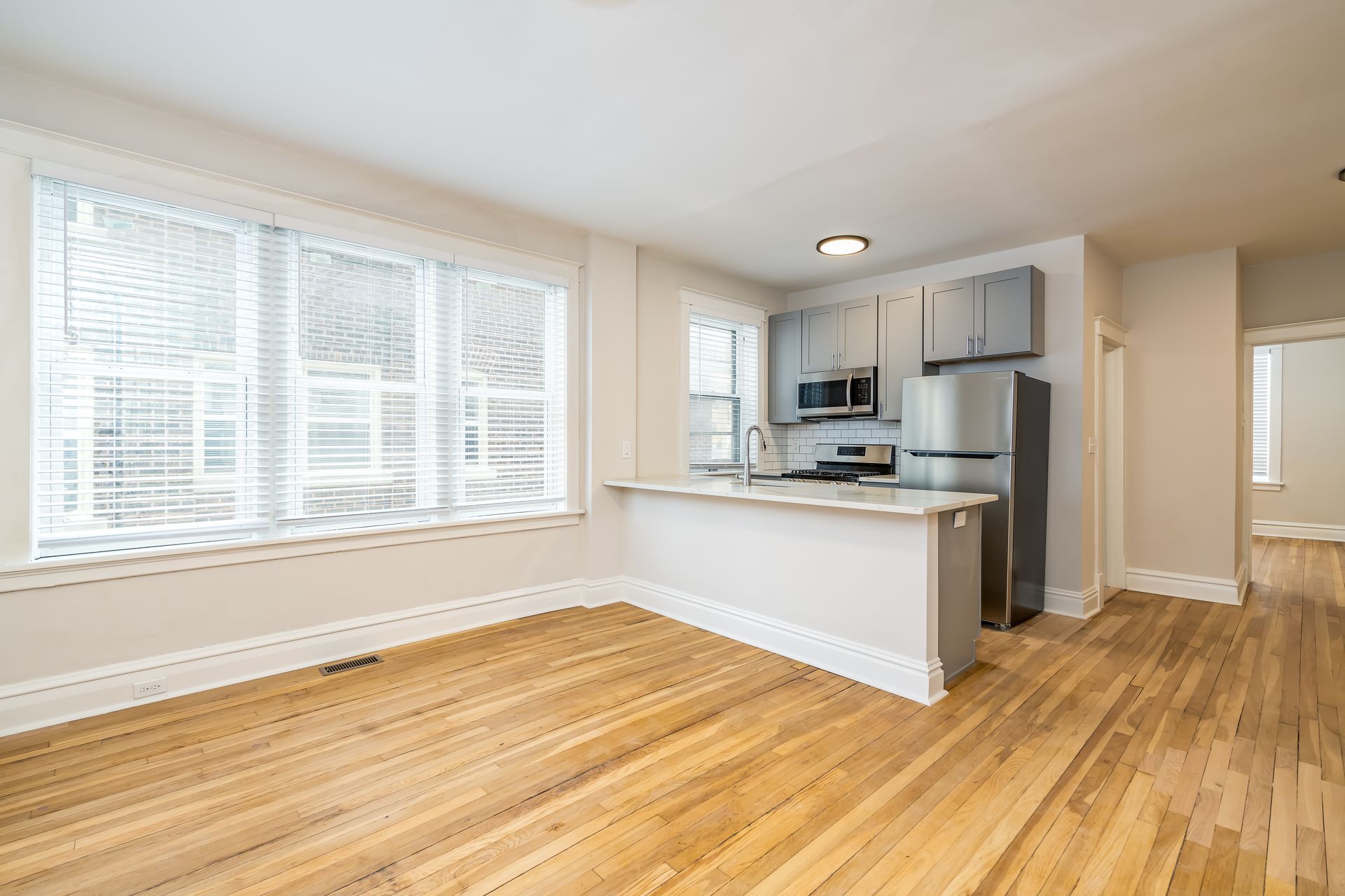 An empty living room with hardwood floors and a kitchen.