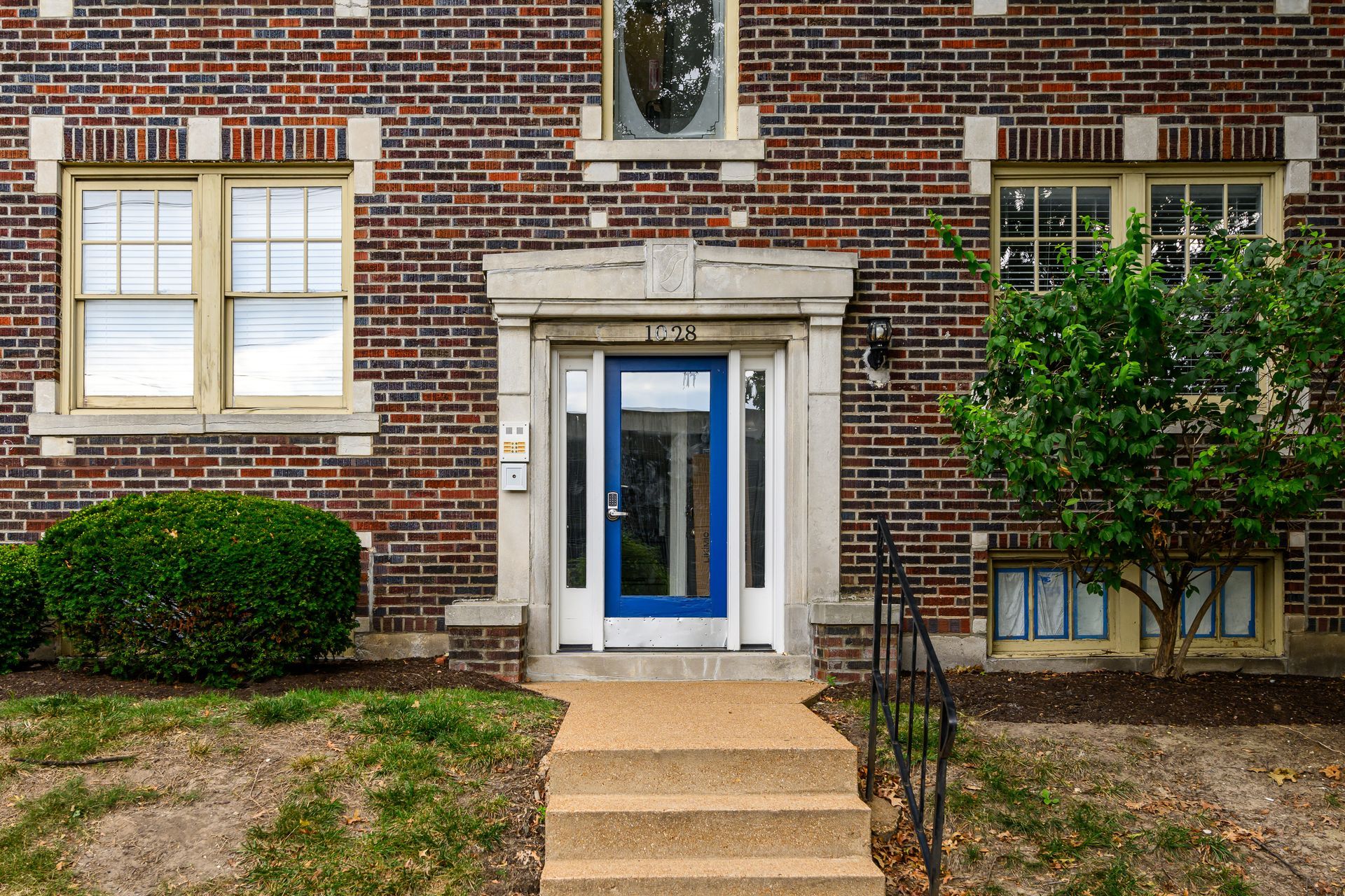 A brick building with a blue door and stairs leading to it.