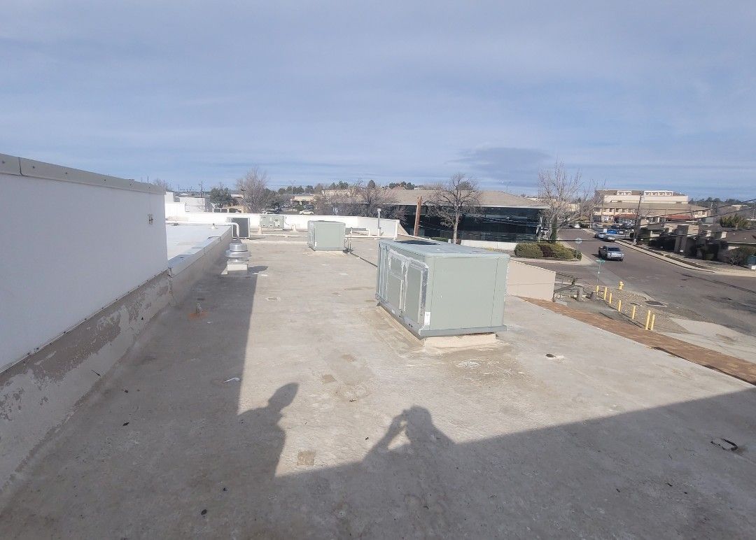 Rooftop with HVAC units and a view of a street and buildings on a sunny day. Shadows of people are visible.