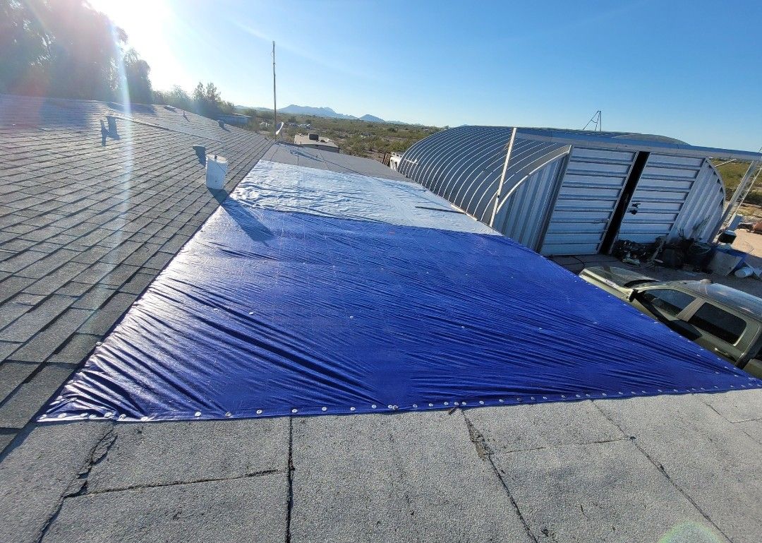 Blue tarp covering a section of a weathered shingle roof, outdoor setting.
