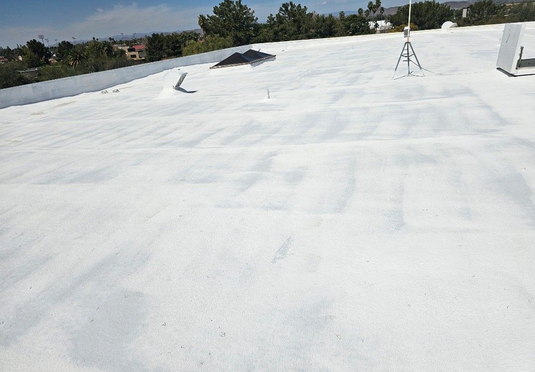 White roof of a building, with a few objects visible: equipment, and some vegetation in the background.