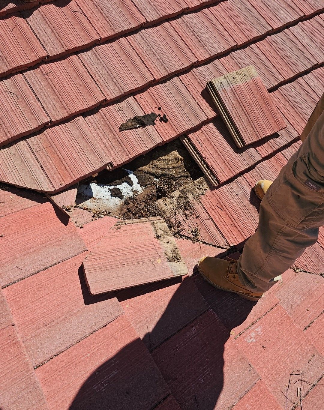 Hole in red tile roof with debris and a person's leg and boot.