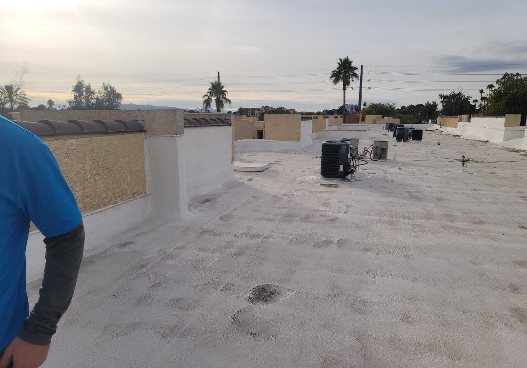 Person on flat white roof with HVAC units, beige walls, and palm trees in the background.