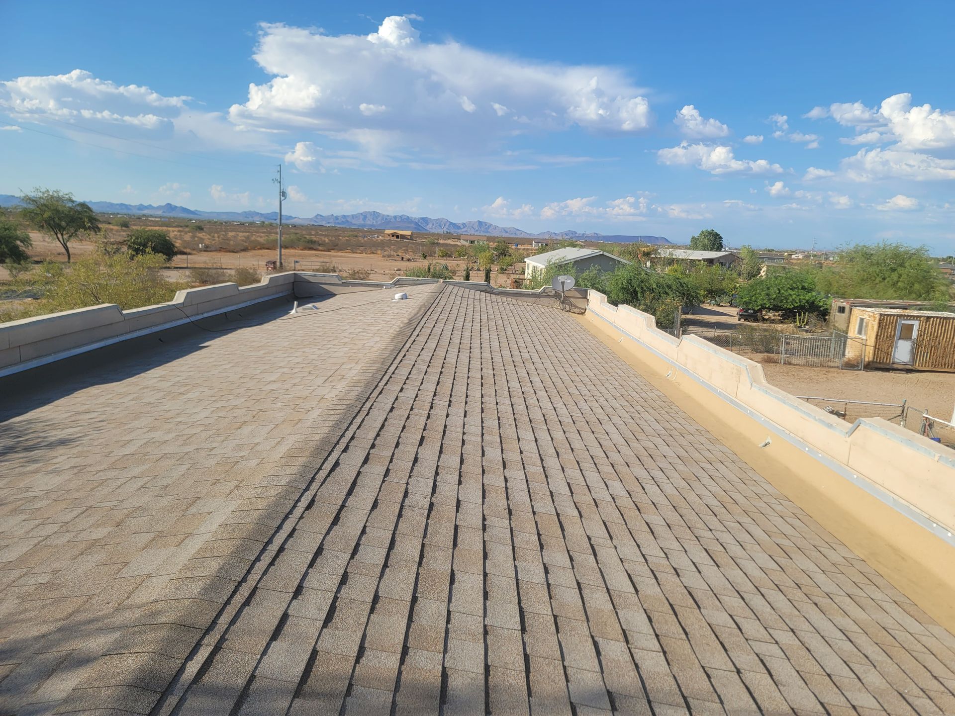 A dirt road with rows of grooves, bordered by low walls, under a blue sky with clouds.