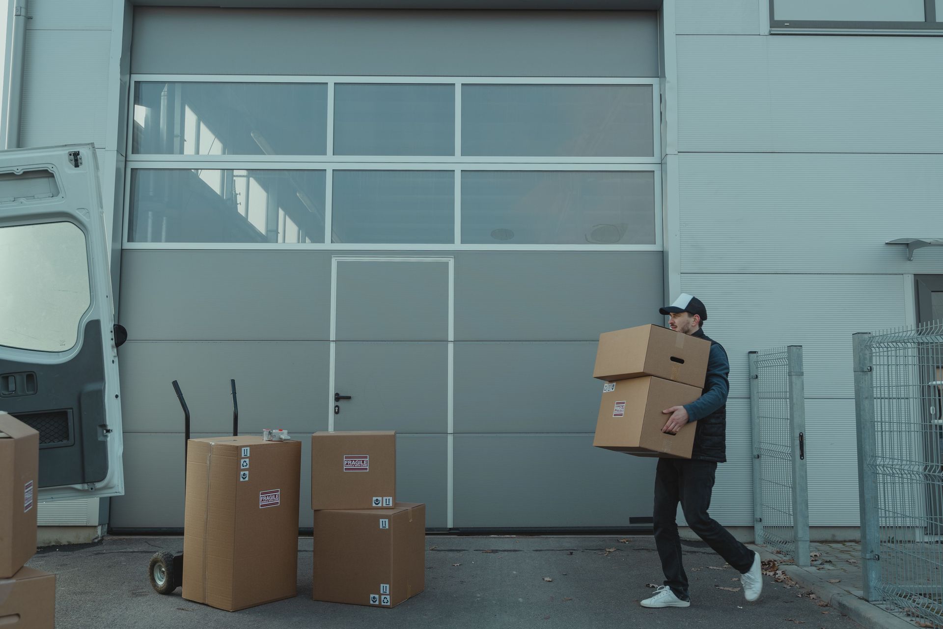 Worker carrying stacked cardboard boxes outside an industrial building