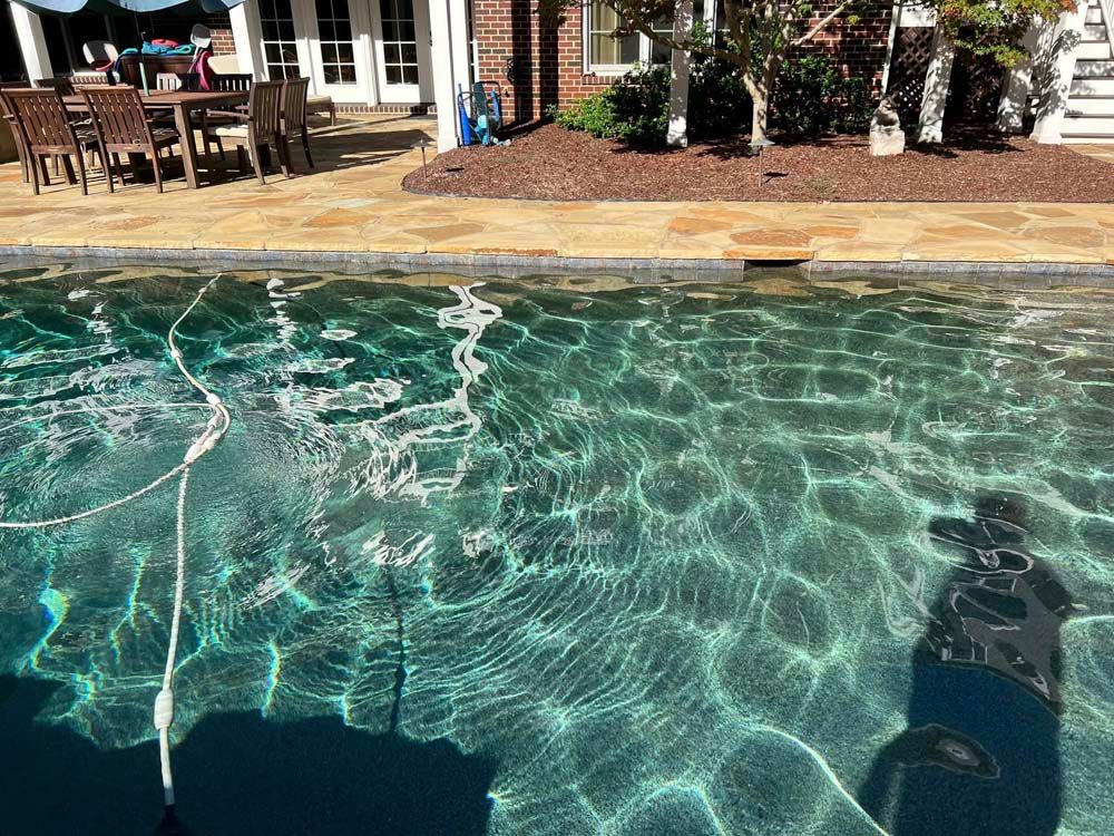 Clear swimming pool with sunlit ripples, patio chairs, and a building in the background
