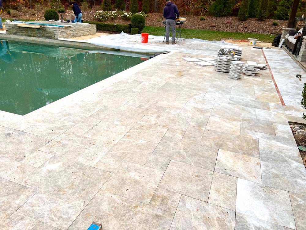 Poolside patio with light stone pavers and workers near a swimming pool