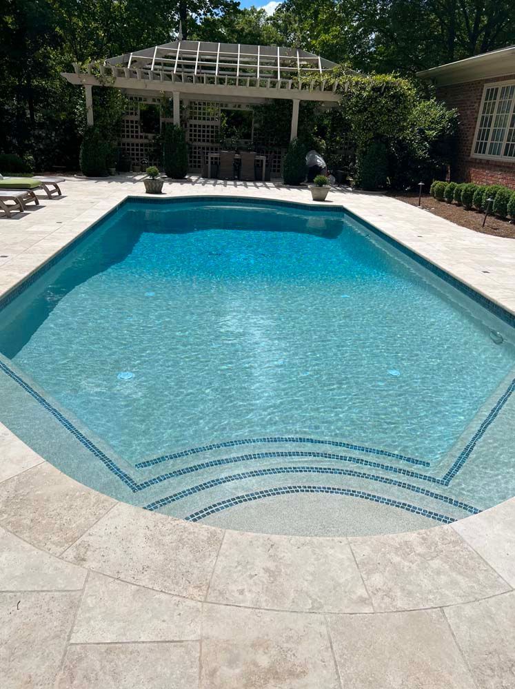 Backyard swimming pool with blue water, stone deck, and shaded patio seating area