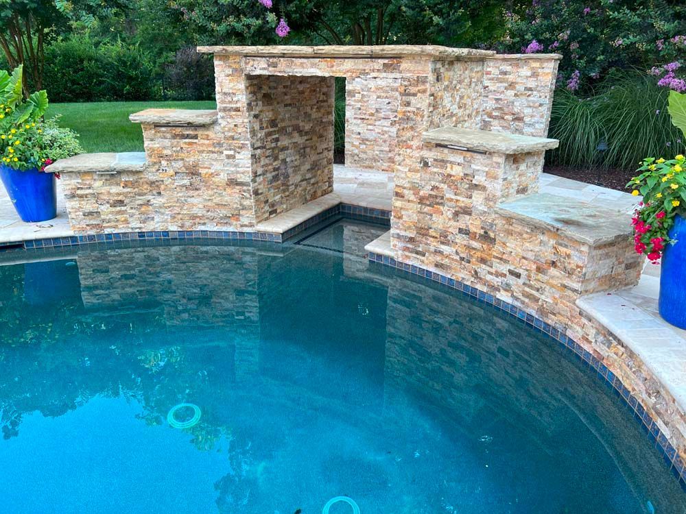 Backyard pool with a stone water feature and surrounding greenery