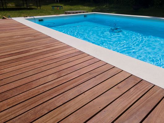 Wooden pool deck beside a blue swimming pool with trees in the background