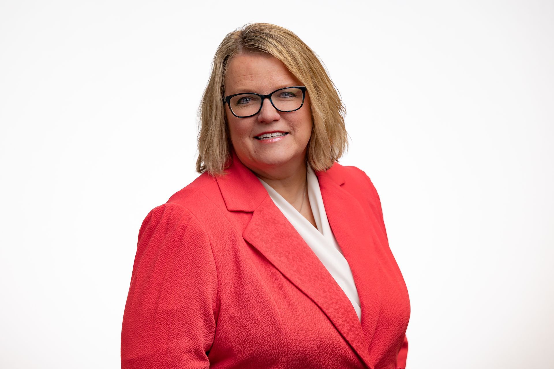 Dr. Celina wearing glasses, smiling, in a red blazer and white shirt, against a white background.