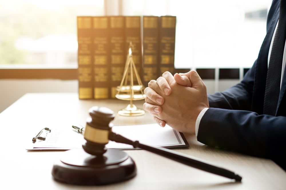 Lawyer’s desk with gavel, scales of justice, and clasped hands beside stacked legal books