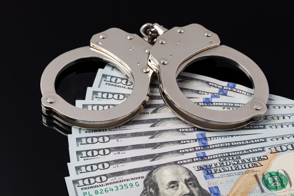 Handcuffs resting on U.S. dollar bills on a dark background