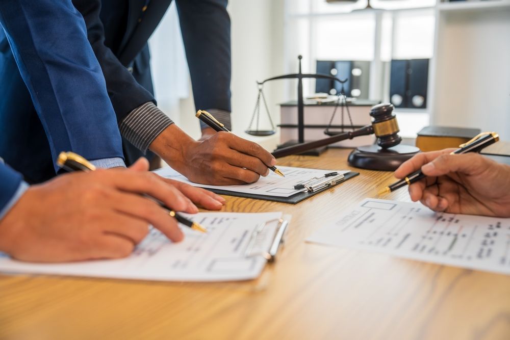 Hands signing documents on a wooden desk during a business meeting, with a gavel and papers nearby