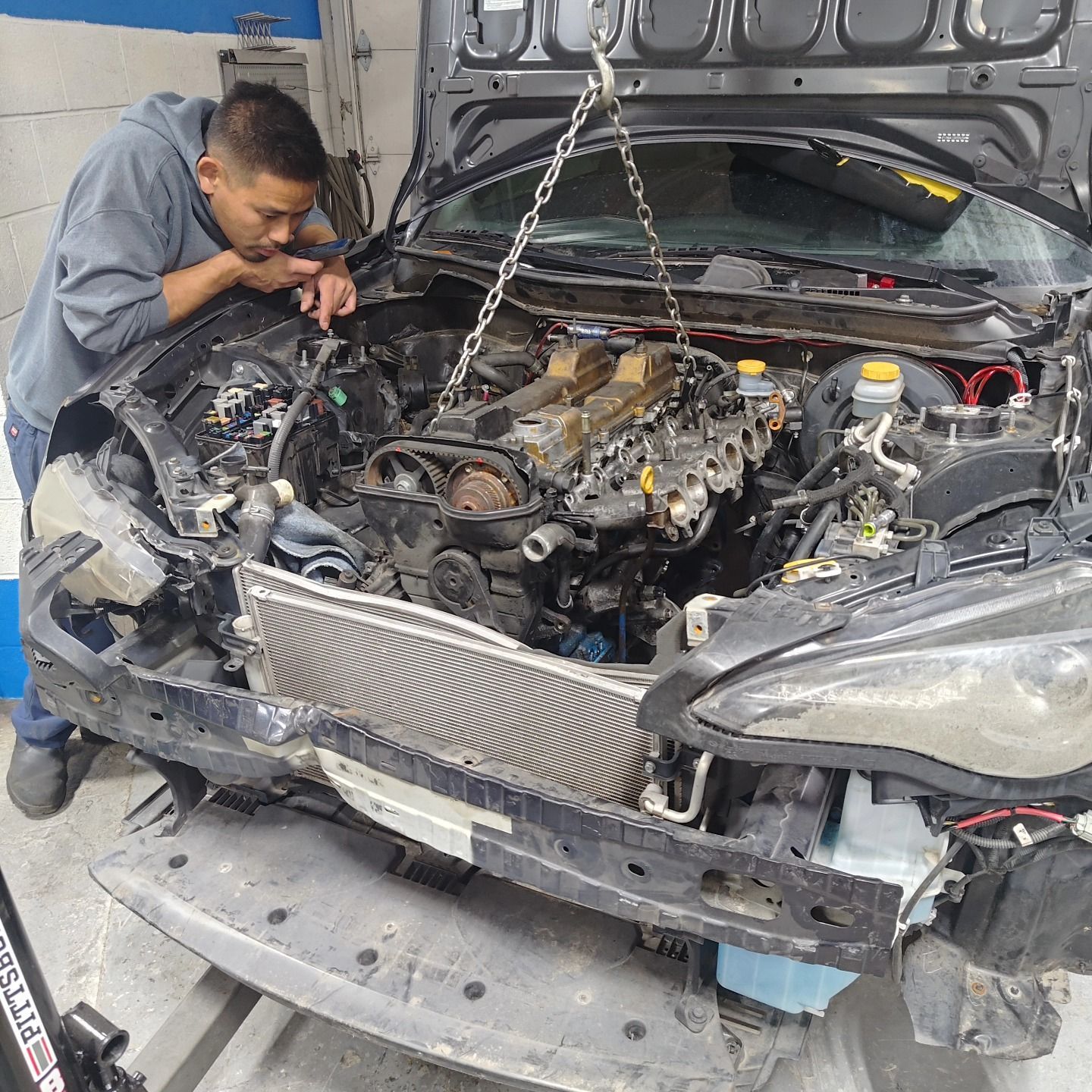 Man leans over a car with its engine being lifted out, in a garage | La Saga Auto