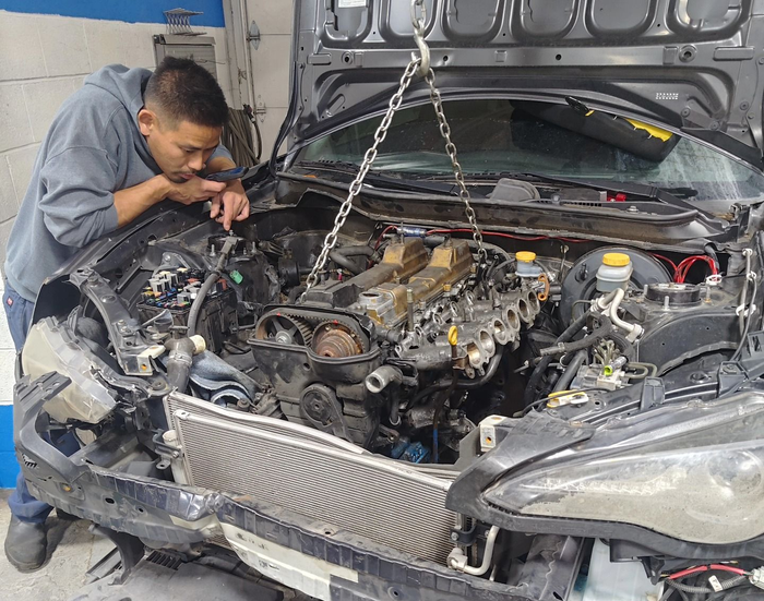 Man inspecting car engine being lifted out with chains in a garage | La Saga Auto