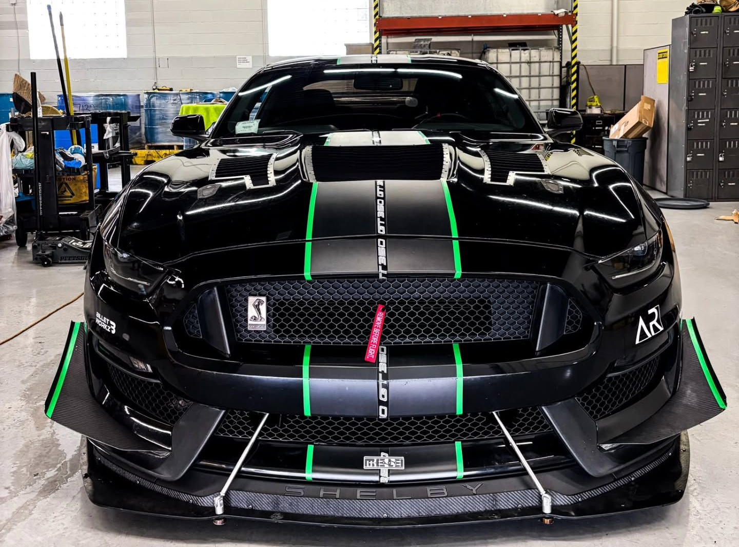 Black Ford Mustang with green racing stripes and modifications, indoors | La Saga Auto