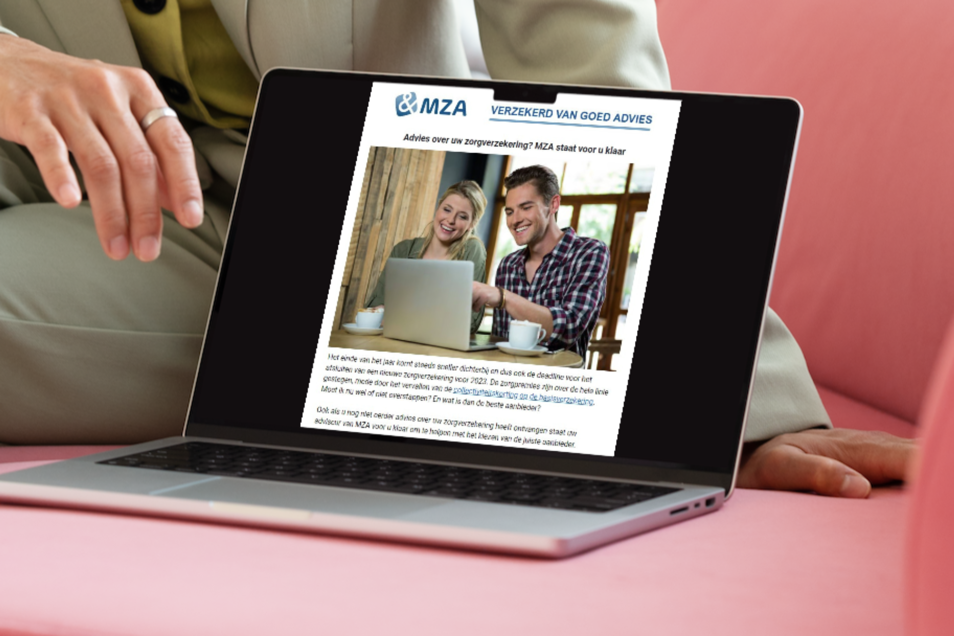 Een persoon zit op een roze bank laat de website van MZA zien op een laptop.