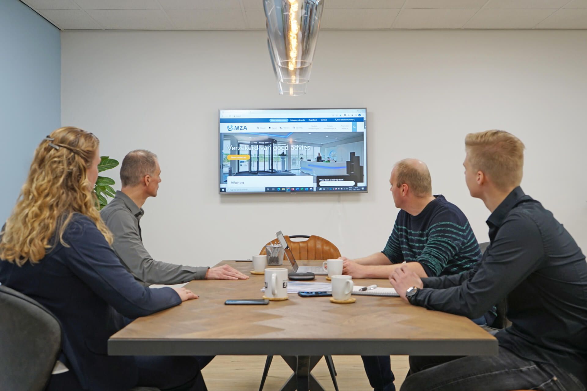 Het team van EAZZI zit aan een tafel voor een televisie.
