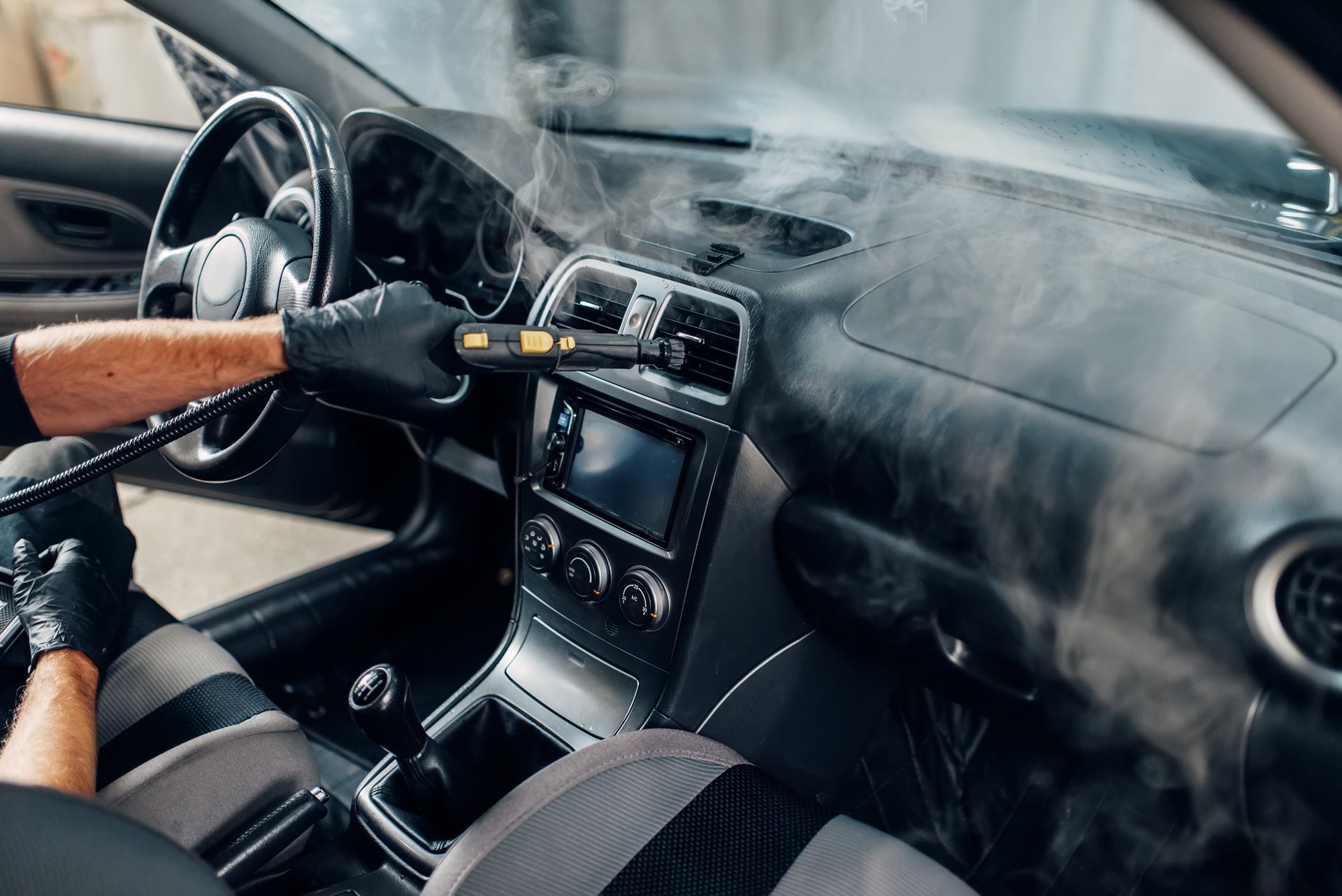 Ein Mann reinigt den Innenraum eines Autos mit einem Dampfreiniger.