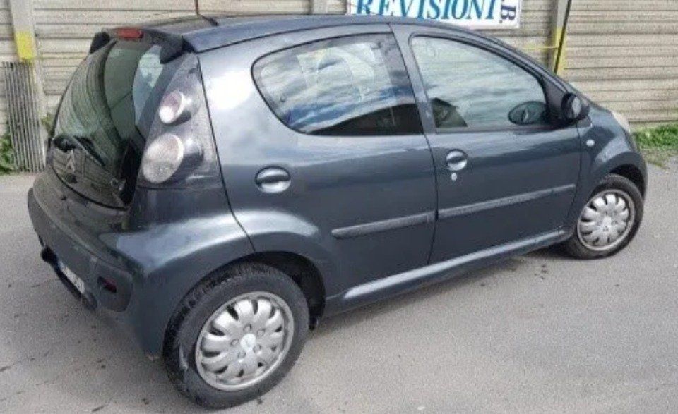 Auto compatta grigia parcheggiata in strada accanto a un edificio, vista posteriore e laterale.
