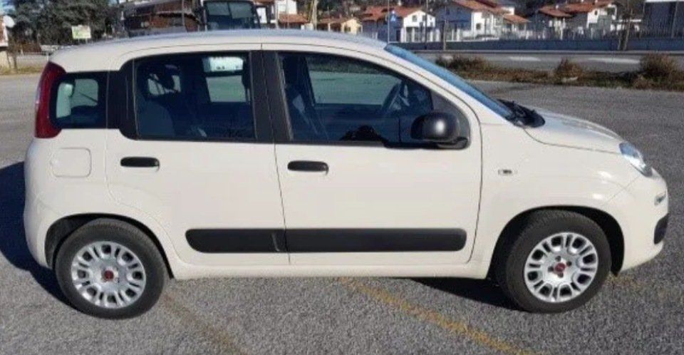 Berlina compatta bianca parcheggiata su un piazzale ghiaioso, vista laterale, con finiture nere e copricerchi argentati.