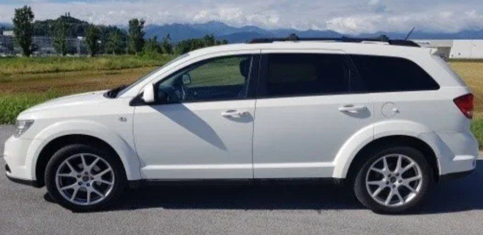 Un SUV bianco parcheggiato su una strada con montagne e campi sullo sfondo.