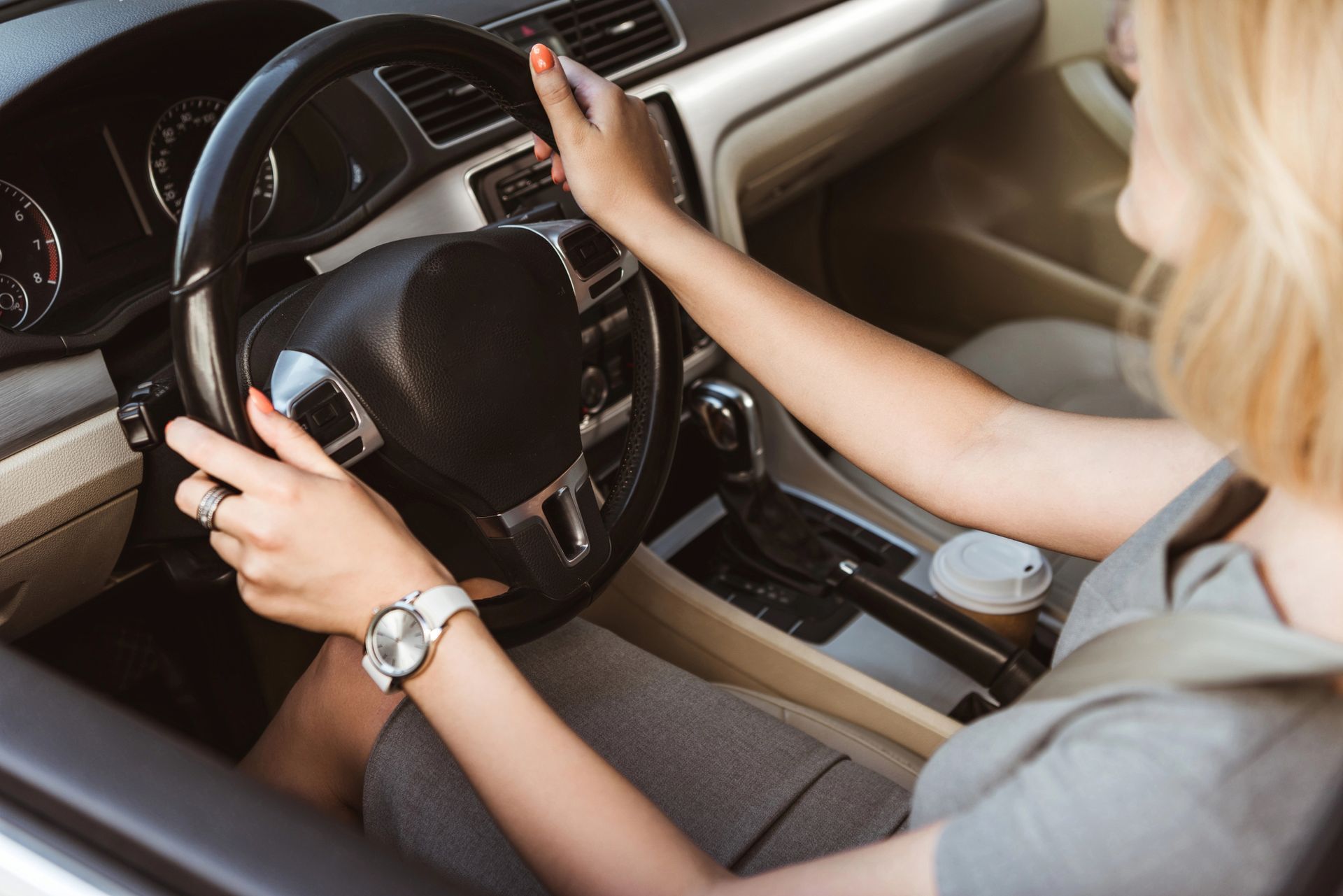 Un guidatore regola il volante all'interno di un abitacolo beige, con una bevanda nella console centrale.